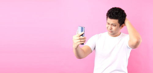  face of Asian man sad shocked what he see in the smartphone isolated on a pink background in studio.