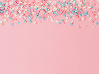 Festive border frame of colorful pastel sprinkles on pink background, copy space top. Sugar sprinkle dots and stars, decoration for cake and bakery. Top view or flat lay