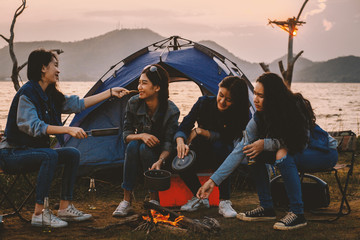 A group of young women camping, they sit around the fire, cook and party together. background it is...