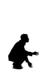 Silhouette of a backlit model posing as a businessman on a white background.  He is crouched on the ground like a detective looking or searching for something on the floor