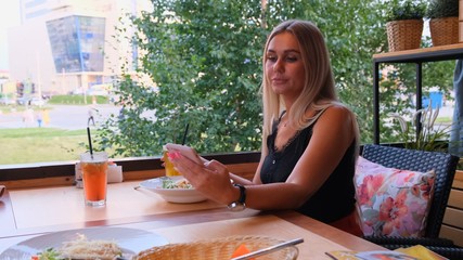 beautiful blonde woman chatting on the phone, talking on skype and drinking a cocktail, sitting in...