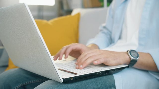 Freelancer seat on sofa in modern living  room and typing on laptop keyboard. Close up 4k slow motion footage.