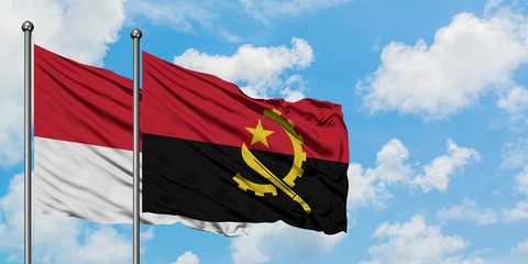 Monaco and Angola flag waving in the wind against white cloudy blue sky together. Diplomacy...