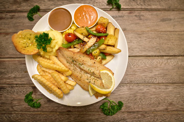 Fish dish - fried fish fillet with fried potatoes and vegetables on wooden rustic background. Top view