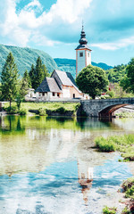 Fototapeta na wymiar Scenery with Church of St John Baptist on Bohinj Lake of Slovenia. Nature in Slovenija. View of blue sky with clouds. Beautiful landscape in summer. Alpine Travel destination. Julian Alps mountains