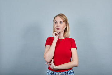 Portrait of pensive young woman in red shirt looking aside, put hand prop up on chin isolated on...