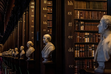 DUBLIN, IRELAND, DECEMBER 21, 2018: The Long Room in the Trinity College Library, home to The Book of Kells. Perspective view of the place, with large quantity of books and chest statues. - obrazy, fototapety, plakaty