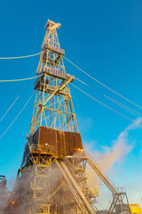 Drilling at a northern oil and gas field in winter. The rig is covered in snow and backlit by the...