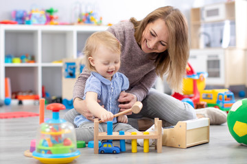 Cheerful baby playing with toys with happy mother in nursery room