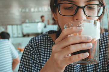 beautiful teen woman drinking cold brew coffee to refreshing in hot summertime at the coffee shop. ice black coffee with lemon is the famous drink in the summer season at the beach cafe.