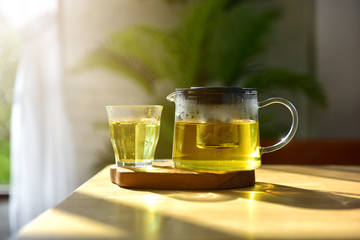 warm soft sunlight falls on a Cup of tea and glass jars on the table. Process and tea ceremony with Hot water is poured from the kettle into a cup with tea leaves.