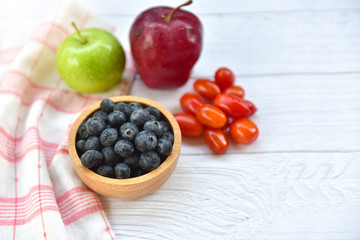 Bowl of fresh blueberries on rustic white wooden table. Healthy organic seasonal fruit background. Organic food blueberries, Cherry tomatoes and Apple for healthy lifestyle. Selected focus. Copy space