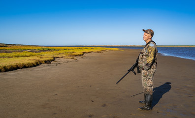 man with a gun stands on the ocean, looks into the distance