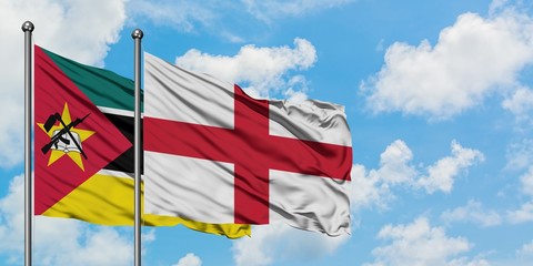 Mozambique and England flag waving in the wind against white cloudy blue sky together. Diplomacy...