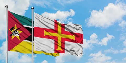 Mozambique and Guernsey flag waving in the wind against white cloudy blue sky together. Diplomacy...