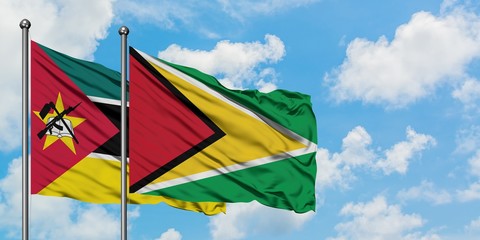 Mozambique and Guyana flag waving in the wind against white cloudy blue sky together. Diplomacy...