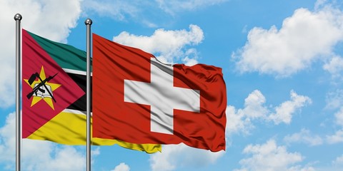Mozambique and Switzerland flag waving in the wind against white cloudy blue sky together....