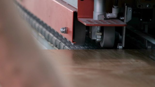 Furniture manufacture. Machine for edging chipboard parts. Worker's hands guide the part for gluing the edge. Close-up. Selective focus. The video contains real production sound and noise.