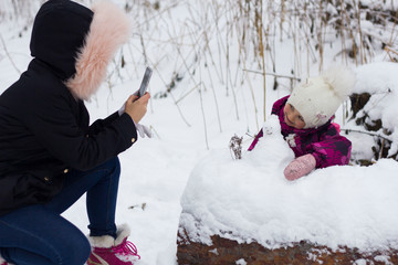 mother takes photo of daughter in winter forest in winter