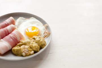 Keto breakfast with fried eggs, bacon, guacamole on white wood table