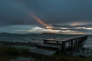 View of a pier on a lake, with a ray of sun against a moody sky
