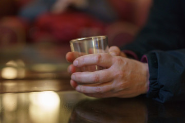 Women hands holding whiskey glass over the table. Photography with defocused background.