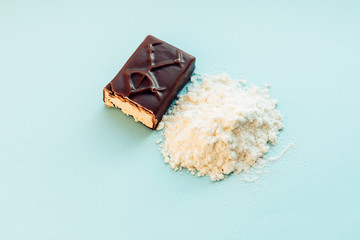 Whey protein powder and energy bar on blue background.