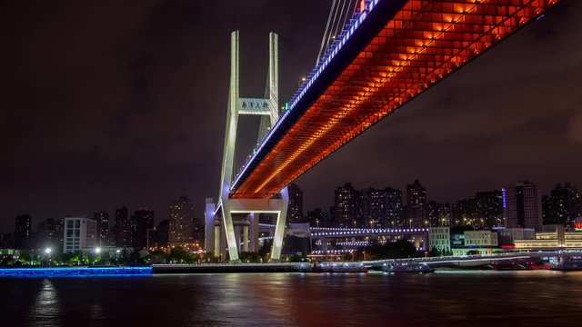 Timelapse famous illuminated Nanpu bridge over Huangpu river reflecting lights against modern Shanghai buildings on bank in China at night