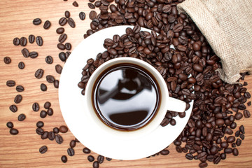 Coffee beans with black coffee on a brown wood background, top view.
