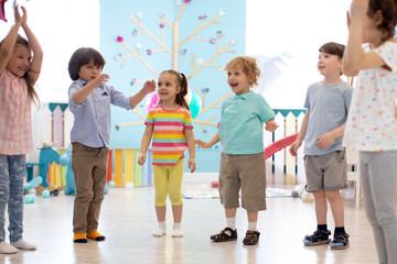Happy children stand semicircle on floor in kindergarten or day care centre. Preschool kids have fun indoors, playing games