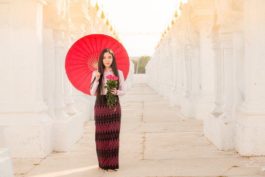 A Asian Myanmar is posing in dresses traditional with a beautiful red rose on special day showing smile face for take photo.