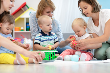 Toddler babies with moms in playroom in nursery