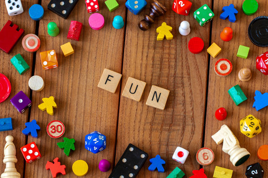 "Fun" spelled out in wooden letter tiles. Surrounded by dice, cards, and other game pieces on a wooden background