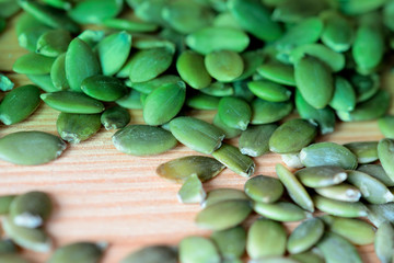 Dry pumpkin seeds scattered on a wooden background close up. Green color toned