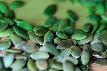 Dry pumpkin seeds scattered on a wooden background close up. Green color toned