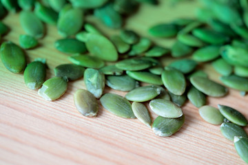 Dry pumpkin seeds scattered on a wooden background close up. Green color toned