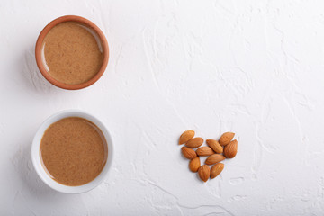Apricot kernel butter smooth, urbech. Natural paste from apricot kernels in white bowls on white table. Top view. Copy space.