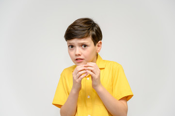 Concept boy teenager shows imitates the behavior of heroes from different movies. Portrait of a child on a white background in a yellow shirt. Standing in front of the camera in poses with emotions.