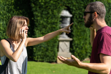 Couple talking to the mobile phone and with angry expression while she points a finger at him