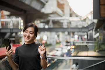 Happy asian woman looking at her phone in the city