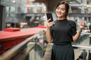 Happy asian woman looking at her phone in the city