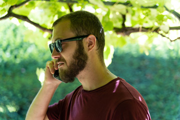 Boy with sunglasses under a grapevine talking on his mobile