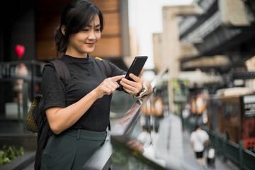 Happy asian woman looking at her phone in the city