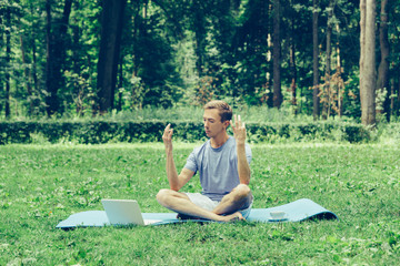 Young attractive white man learns to meditate in the park in front of a laptop.