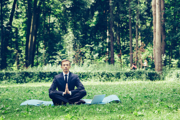 Man in a suit with tie. Business man relaxing in a park in the lotus position, he can't relax in...