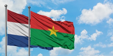 Netherlands and Burkina Faso flag waving in the wind against white cloudy blue sky together....