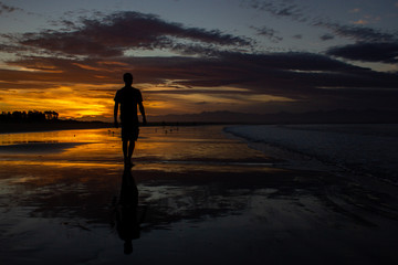 Fototapeta na wymiar silhouette of a young man waling on the beach in nelson during sunset on Tahunanui Beach at Nelson, New Zealand