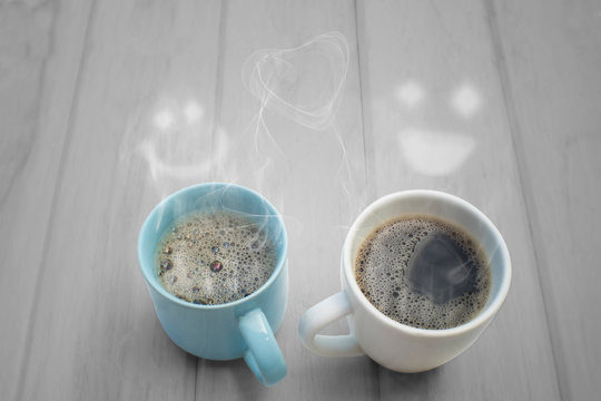 Two hot coffee and steam smiling faces on wood table.