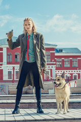 A handsome young guy in a khaki and berets military coat walks with a big dog. Holds a flask in his...
