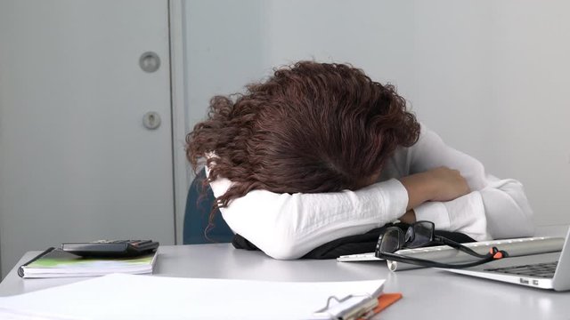 Tired employee or office executive sleeping on her office desk in front of her computer. Overwork or tired from work concept.